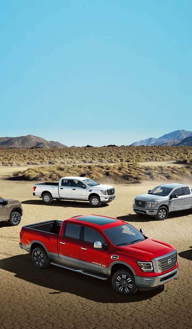 Multiple Nissan pick-up trucks are parked on a desert terrain.