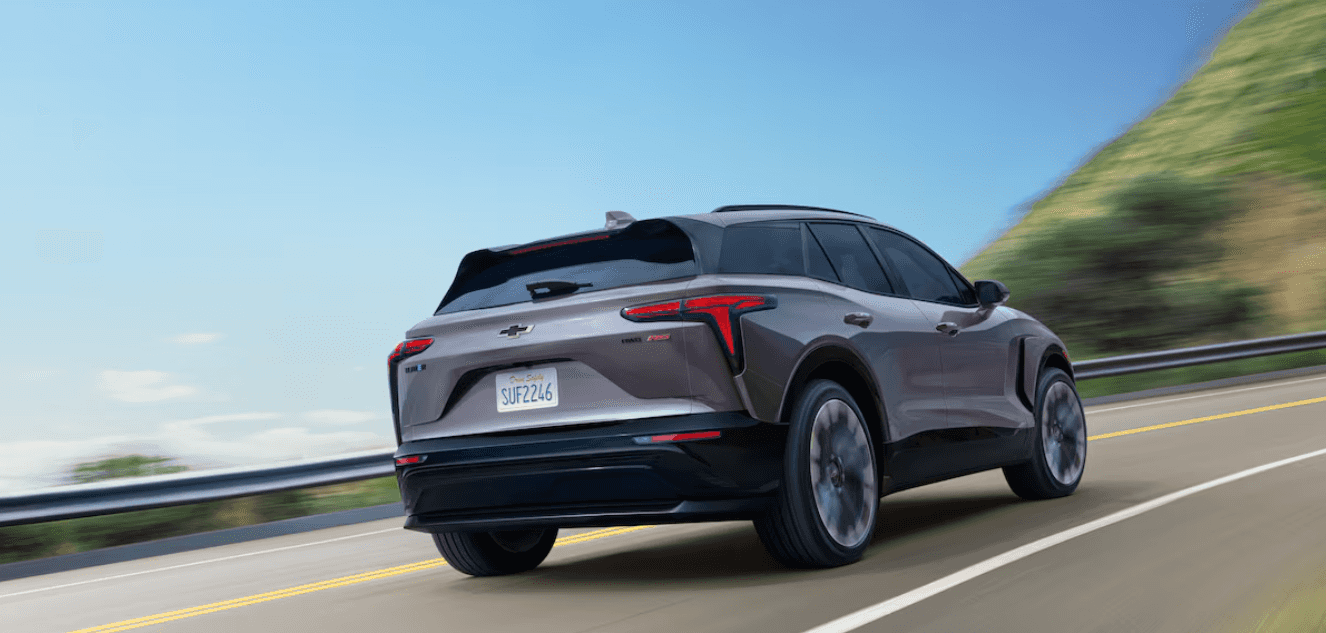 A gray 2025 Chevy Blazer EV drives around a curve on a hilly highway