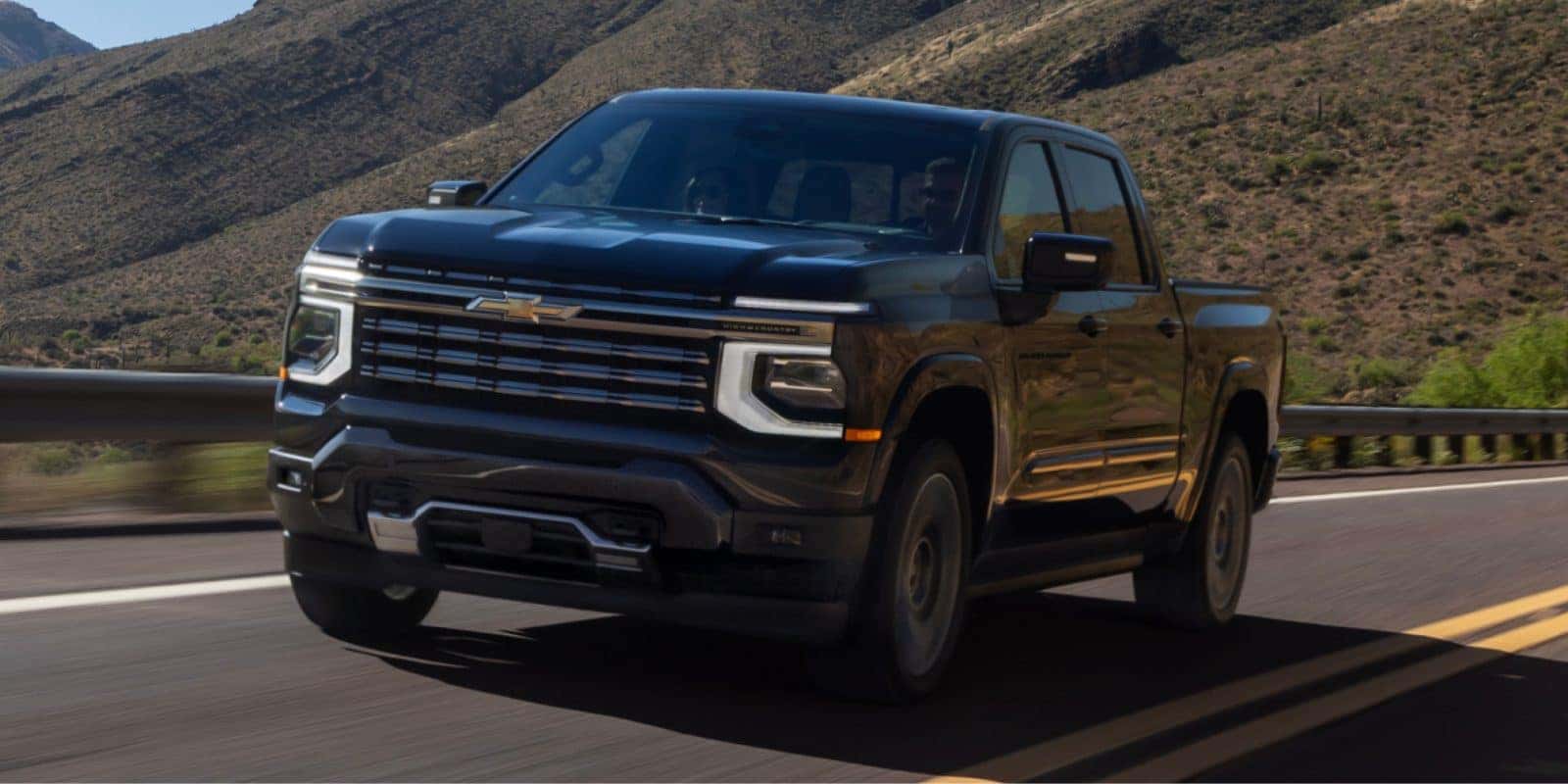 2027 Chevy Silverado 1500 High Country on a mountain highway, compared with the Ram 1500