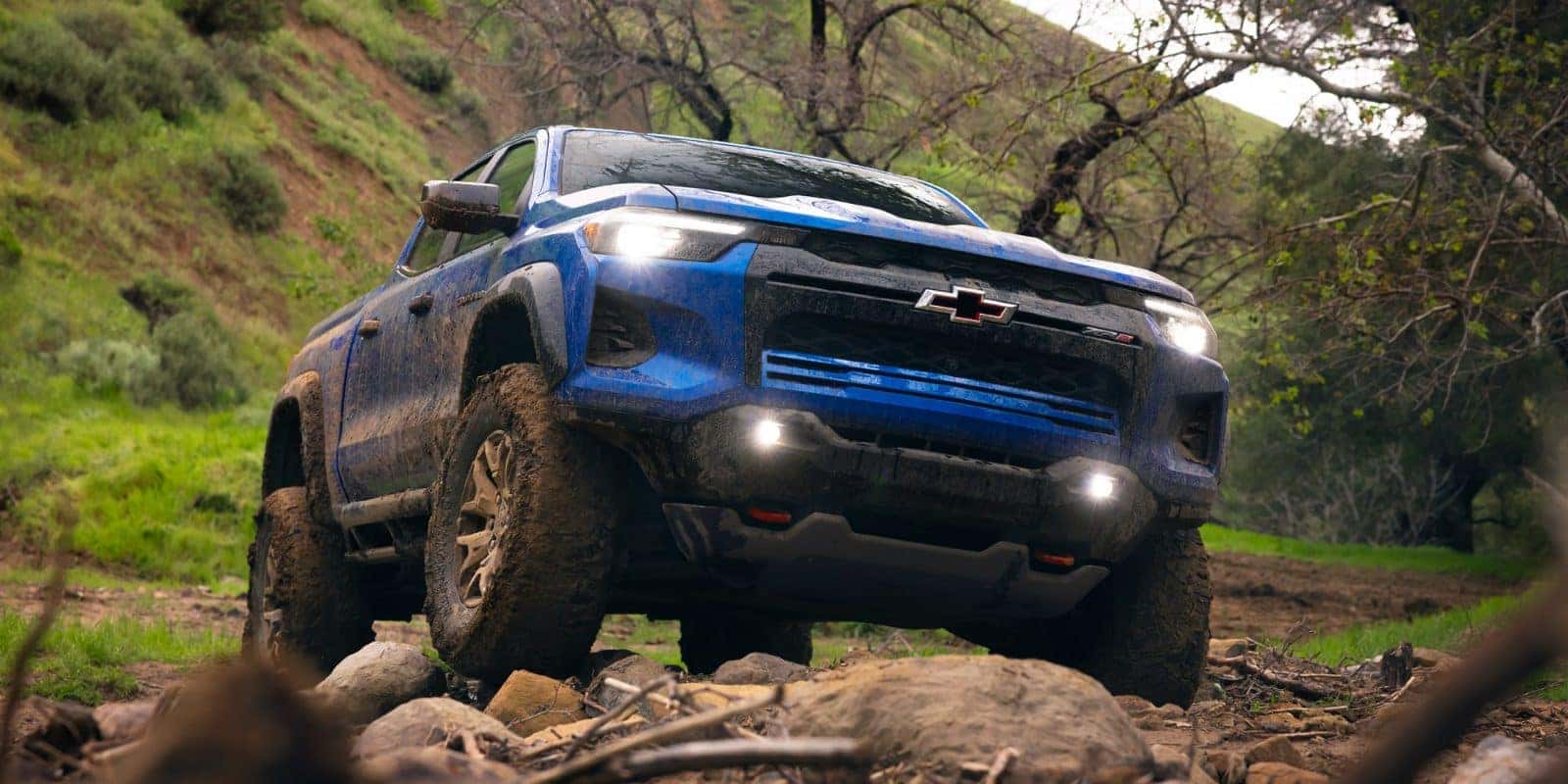 Blue 2026 Chevy Colorado crawling over rocks on a forest trail