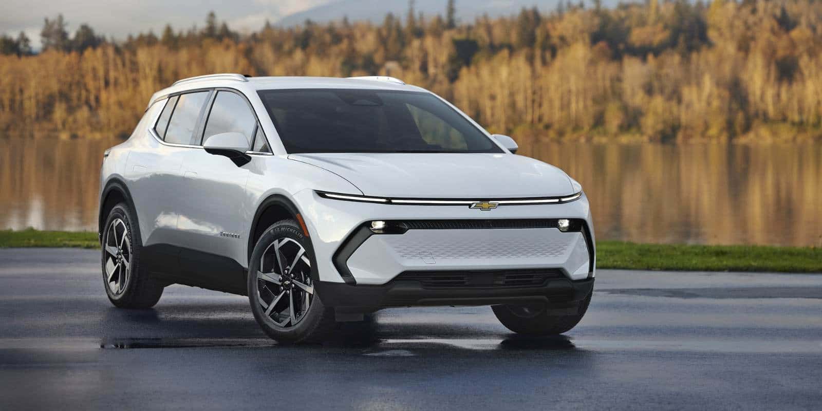 White Chevy Equinox EV parked by a lake with autumn trees