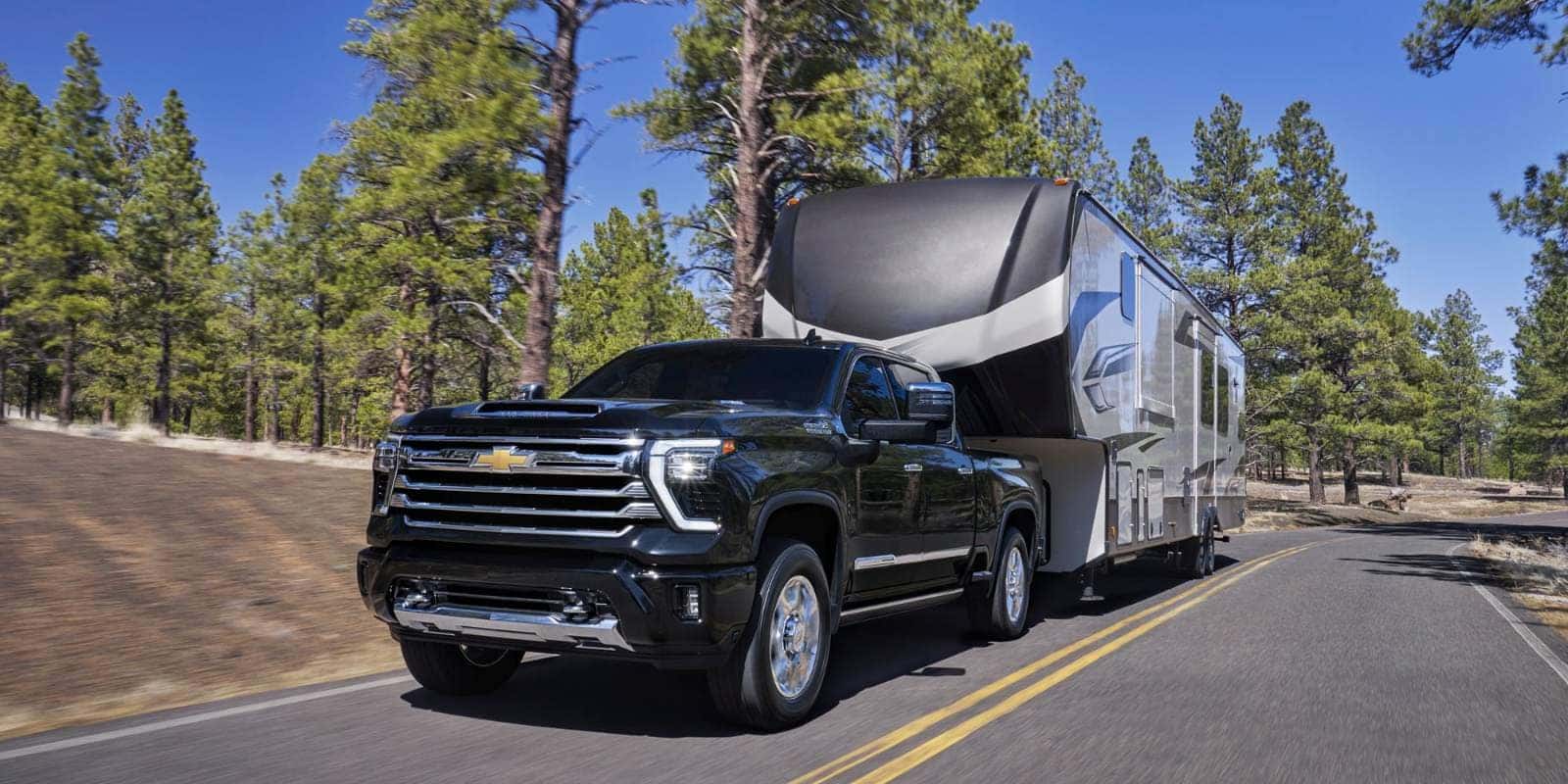 2026 Chevy Silverado HD towing a fifth-wheel camper on a forest road