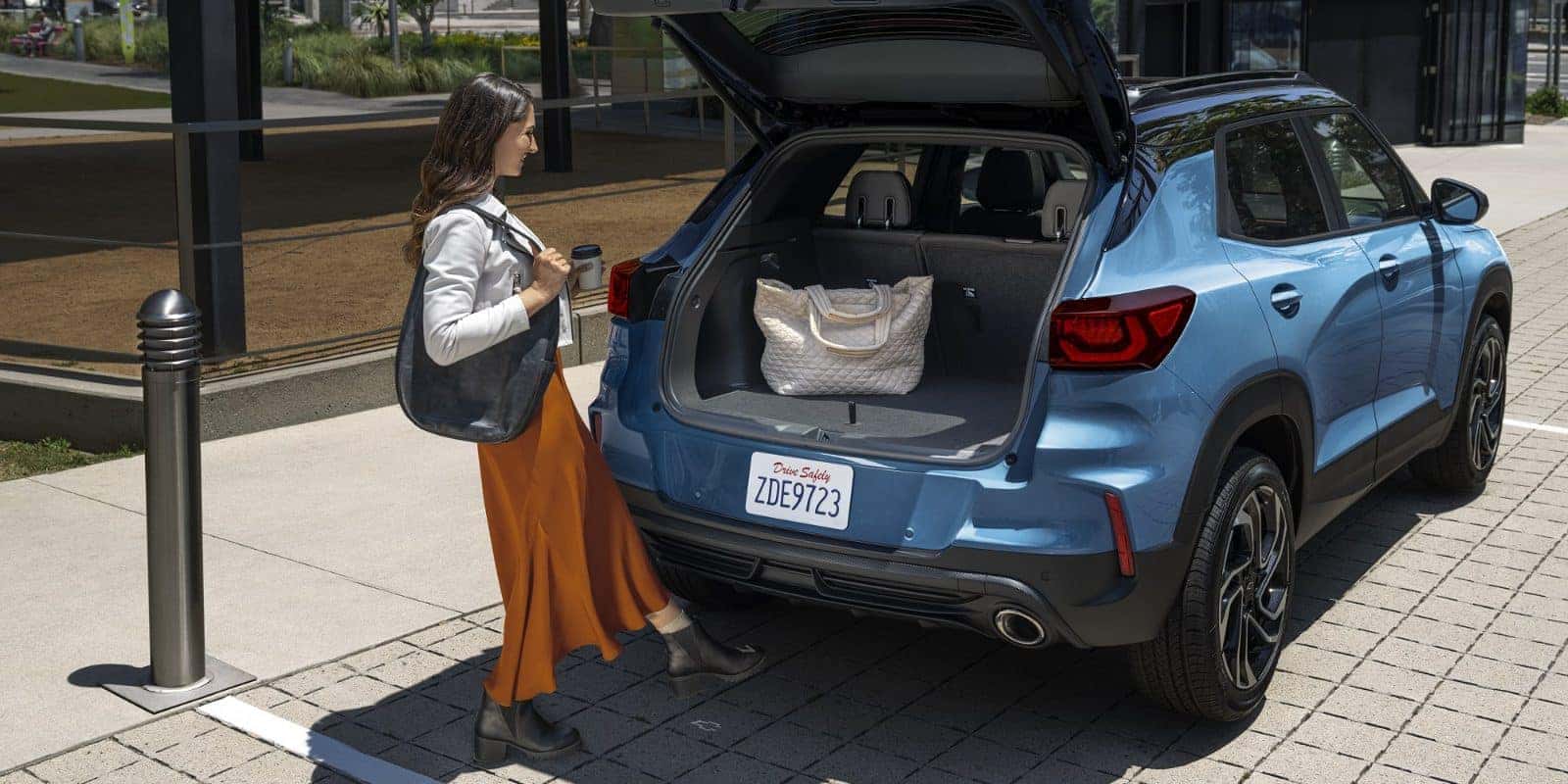 Woman loading a bag into the cargo area of a blue Chevy Trailblazer