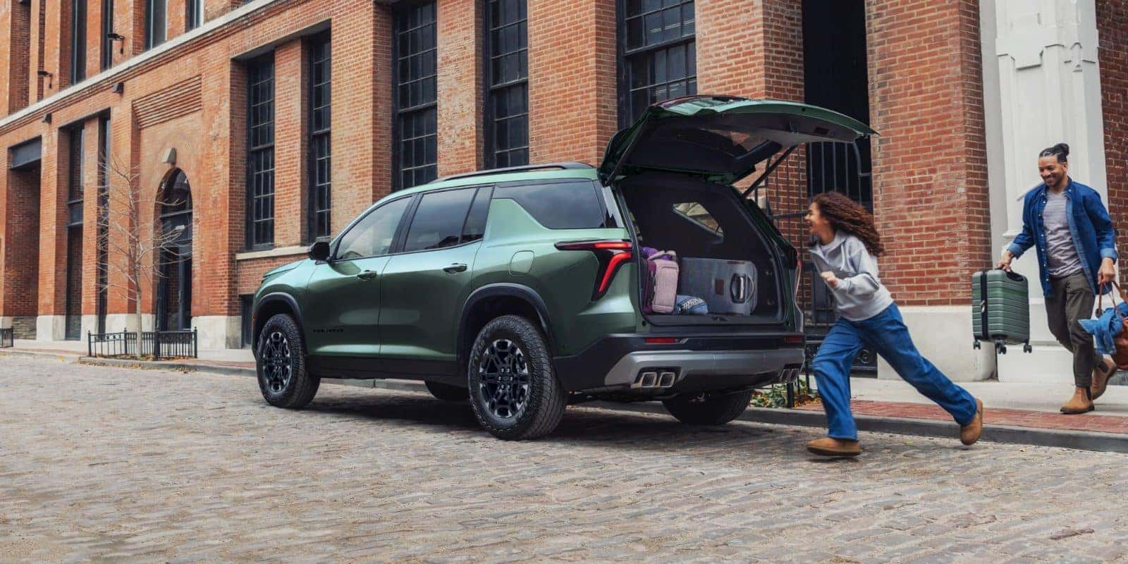 Family loading luggage into the cargo area of a green Chevy Traverse