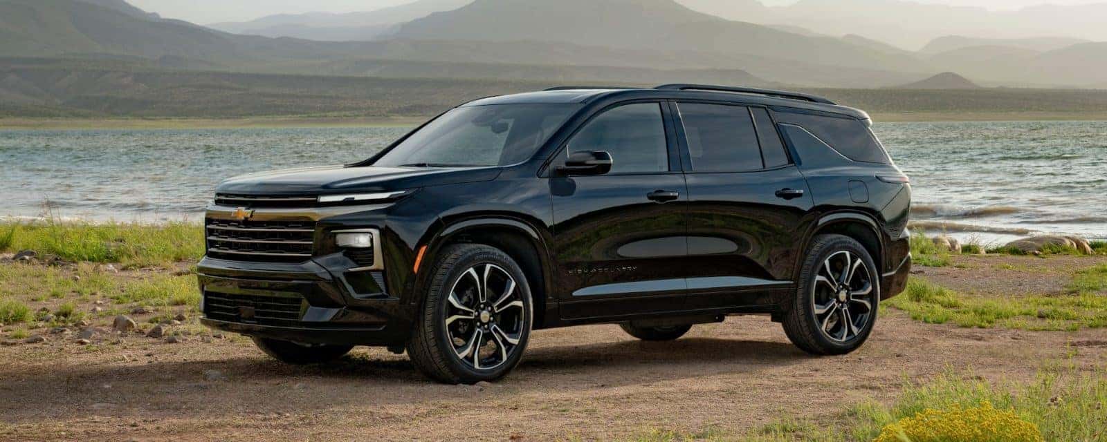 Black Chevy Traverse parked beside a lake with mountains behind