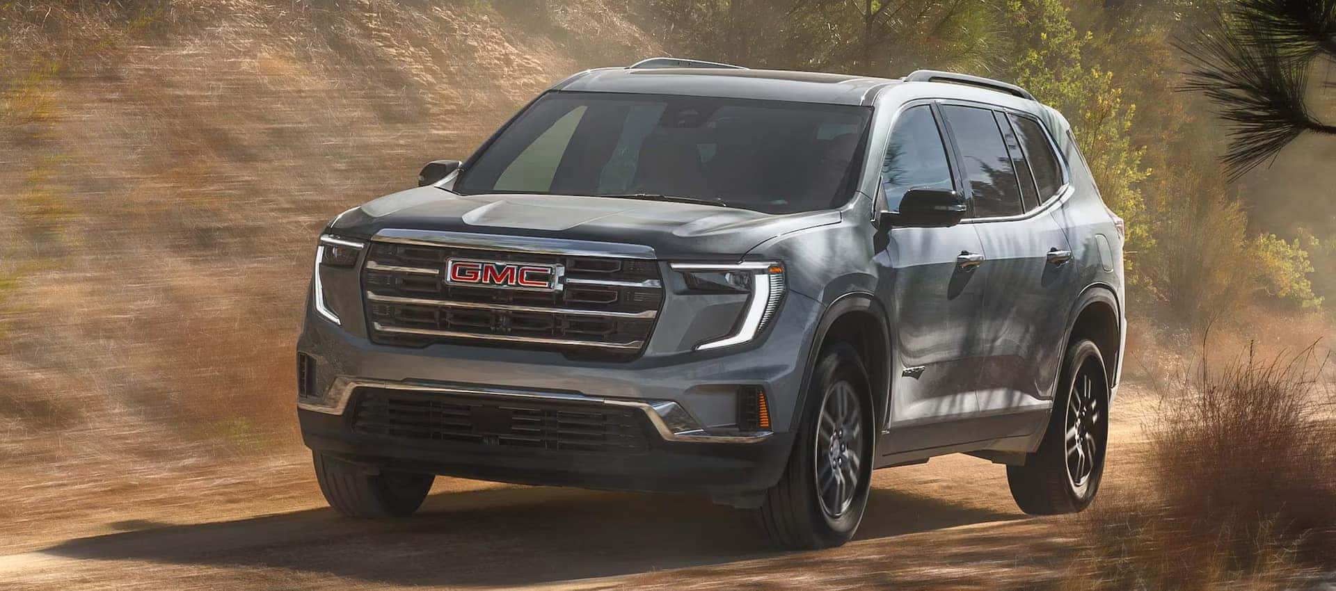 2027 GMC Acadia driving through a dusty off-road trail