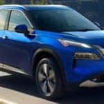 A blue 2021 Nissan Rogue is driving on a winding road after leaving a Hendersonville Nissan dealer.