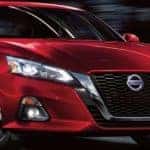 A red 2021 Nissan Altima is driving on a city street at night.
