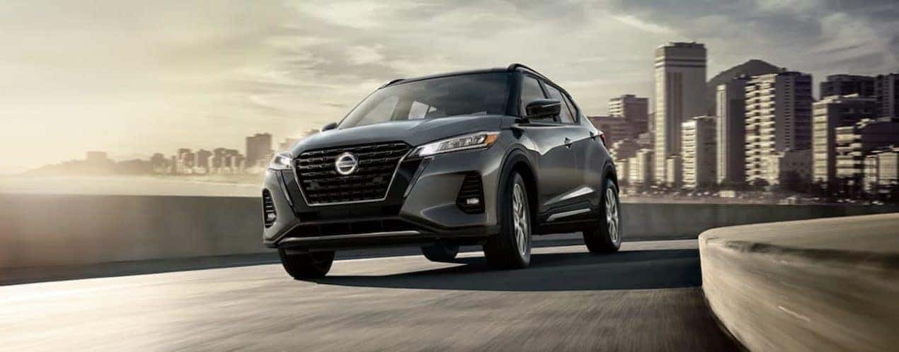 A grey 2021 Nissan Kicks is driving away from a city.