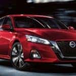 A red 2021 Nissan Altima is driving through a city at night after leaving a White House TN Nissan dealership.