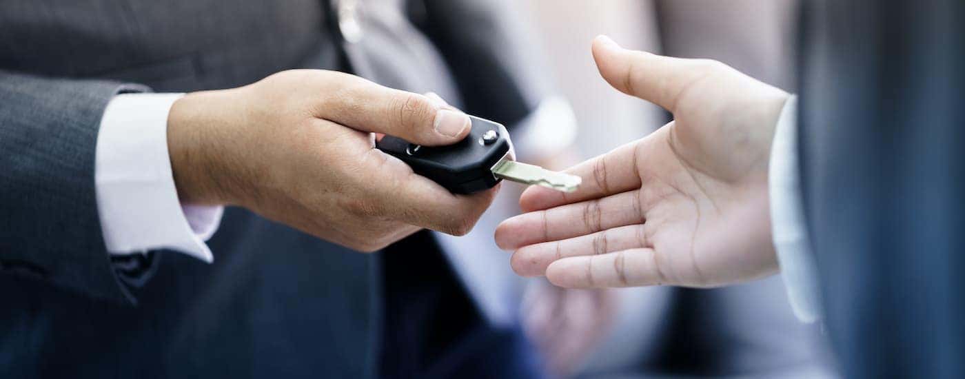 A salesman is passing a set of keys to someone at a car dealership.