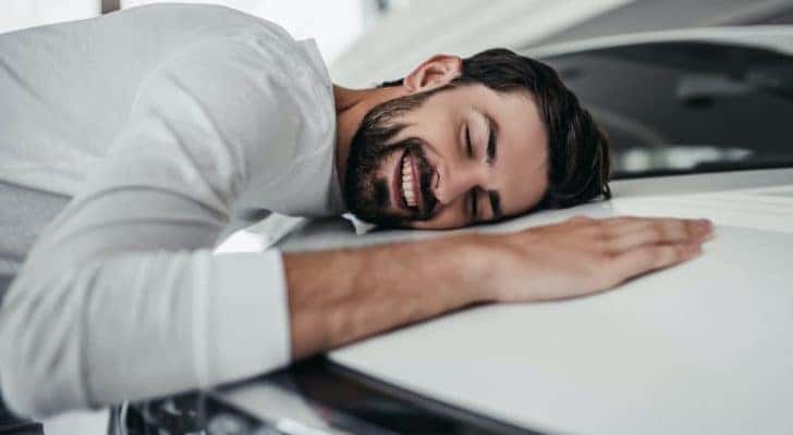 A man is laying on a car after looking at new cars in stock.