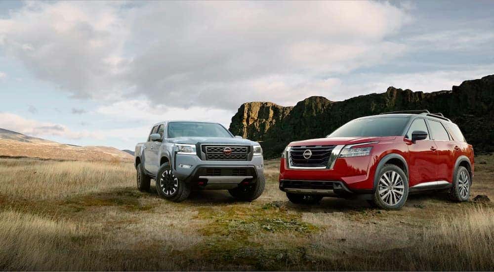 A grey 2022 Nissan Frontier is shown next to a red Pathfinder in a field.