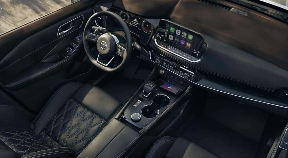 The black and silver accented interior of a 2022 Nissan Rogue shows the steering wheel and center console.