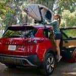 A woman is shown securing a kayak to the roof of a red 2022 Nissan Rogue.