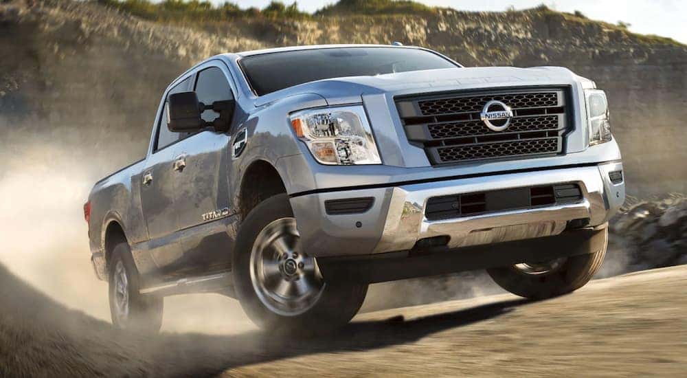 A silver 2021 Nissan Titan XD is shown driving on a dusty road after leaving a Nissan Titan dealer.