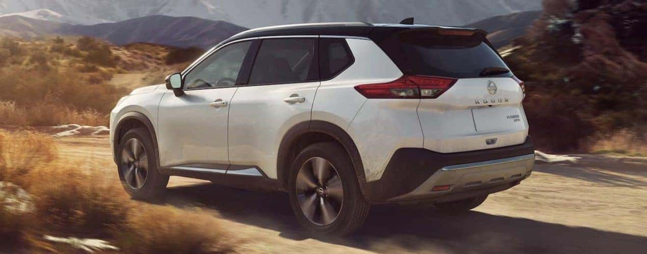A white 2022 Nissan Rogue is shown from the rear driving on a dirt road.