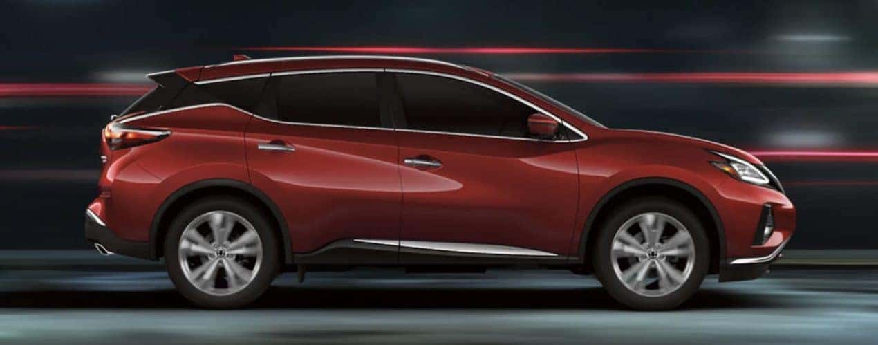 A red 2022 Nissan Murano is shown from the side driving on a city street at night.