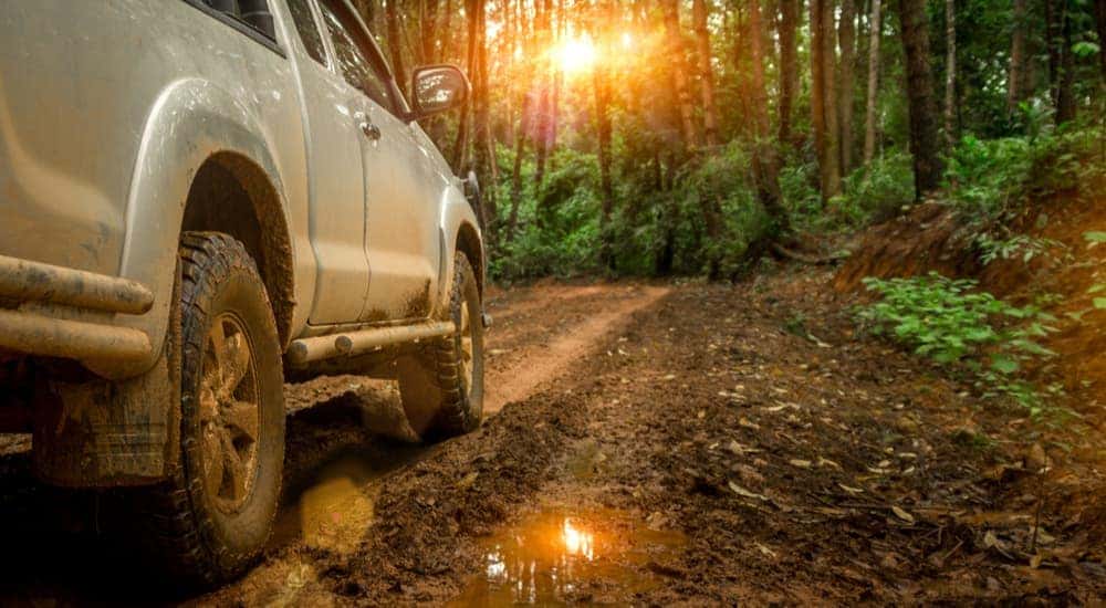 A grey truck is shown from the side while driving on a muddy trail.