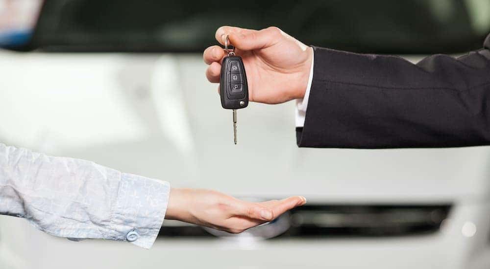 A person is shown passing their car keys to a salesperson after searching "sell my car."