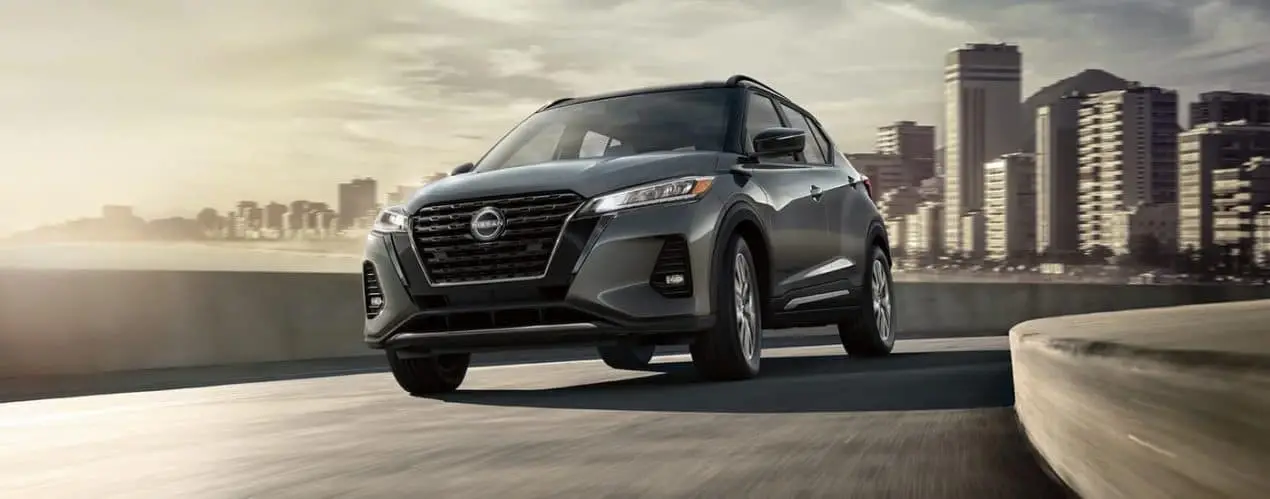 A grey 2022 Nissan Kicks is shown driving on a highway near a city.