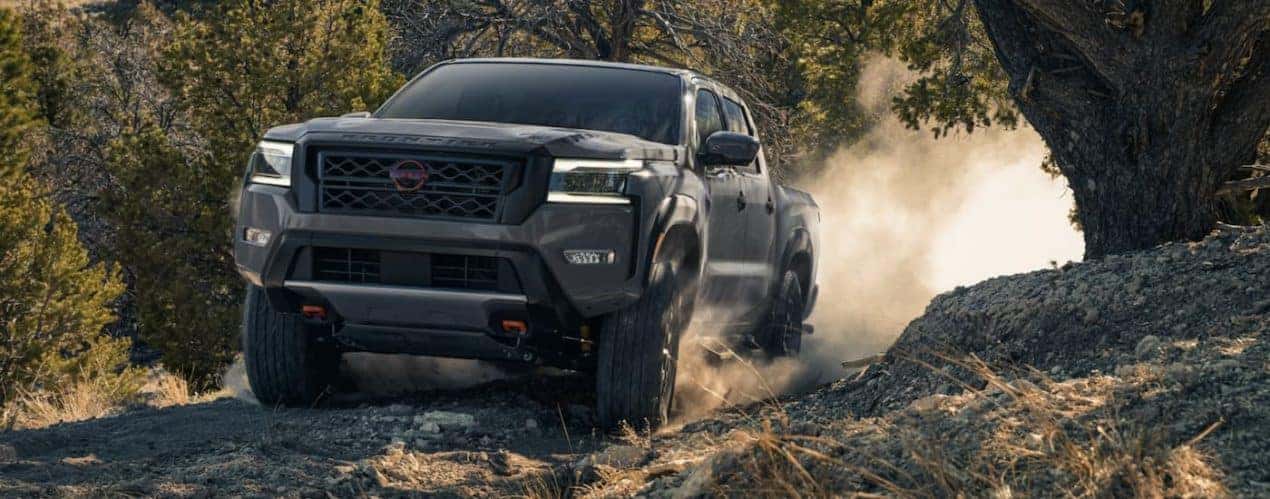 A grey 2022 Nissan Frontier is shown from the front off-roading on a dirt path during a 2022 Nissan Frontier vs 2022 Chevy Colorado comparison.