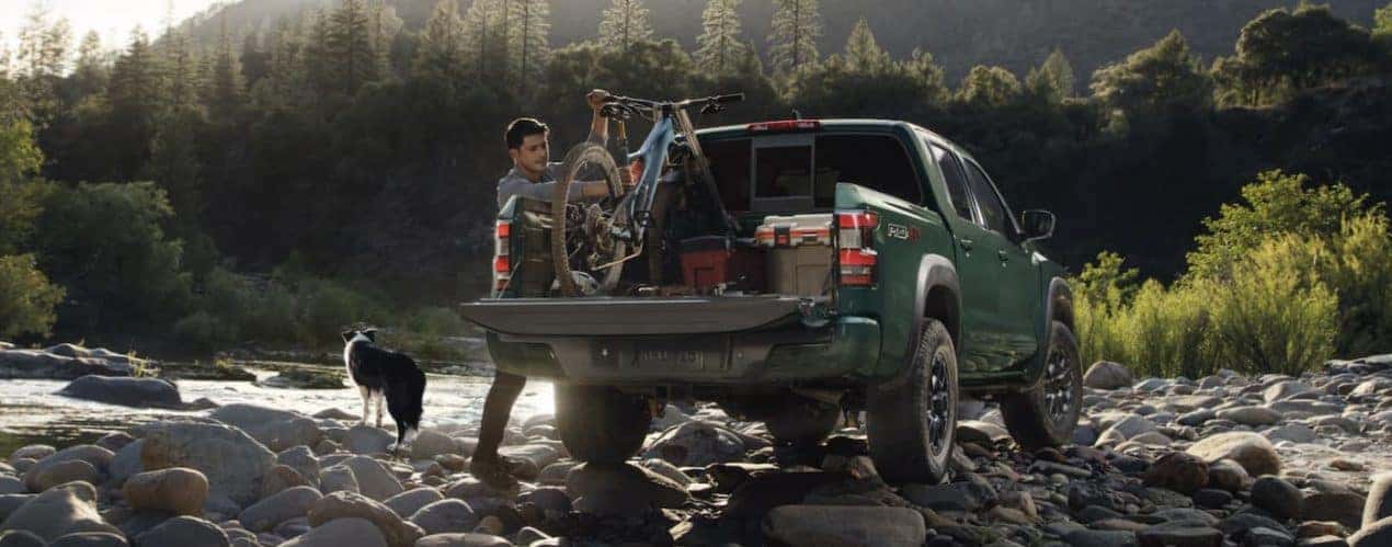 A green 2022 Nissan Frontier is shown from the rear parked on a river bank.