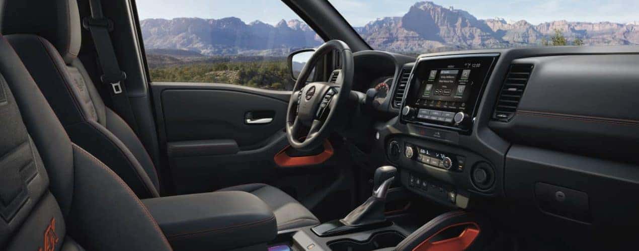 The black interior of a 2022 Nissan Frontier shows the steering wheel and infotainment screen.