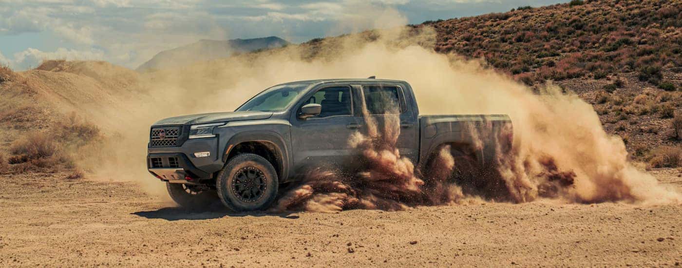 A grey 2022 Nissan Frontier is shown from the side kicking up sand after leaving a lifted truck dealer.