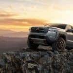 A grey 2022 Nissan Frontier Pro-4x is shown from the front while it climbs over rocks after leaving a lifted truck dealer.