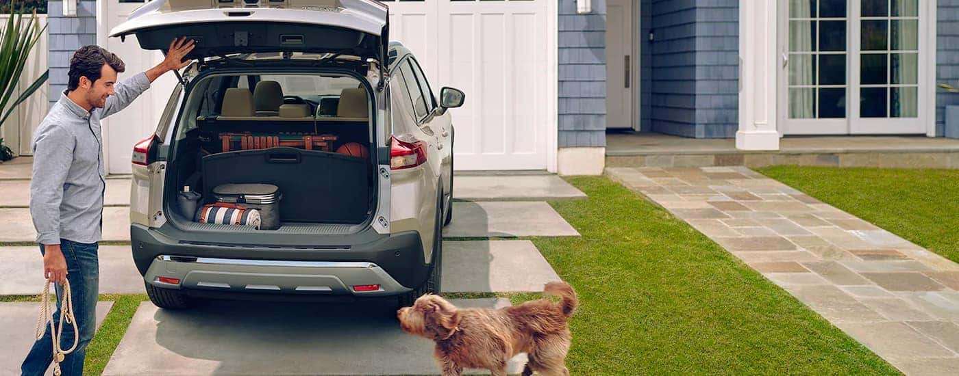 A grey 2021 Nissan Rogue is shown in a driveway near a dog and person.