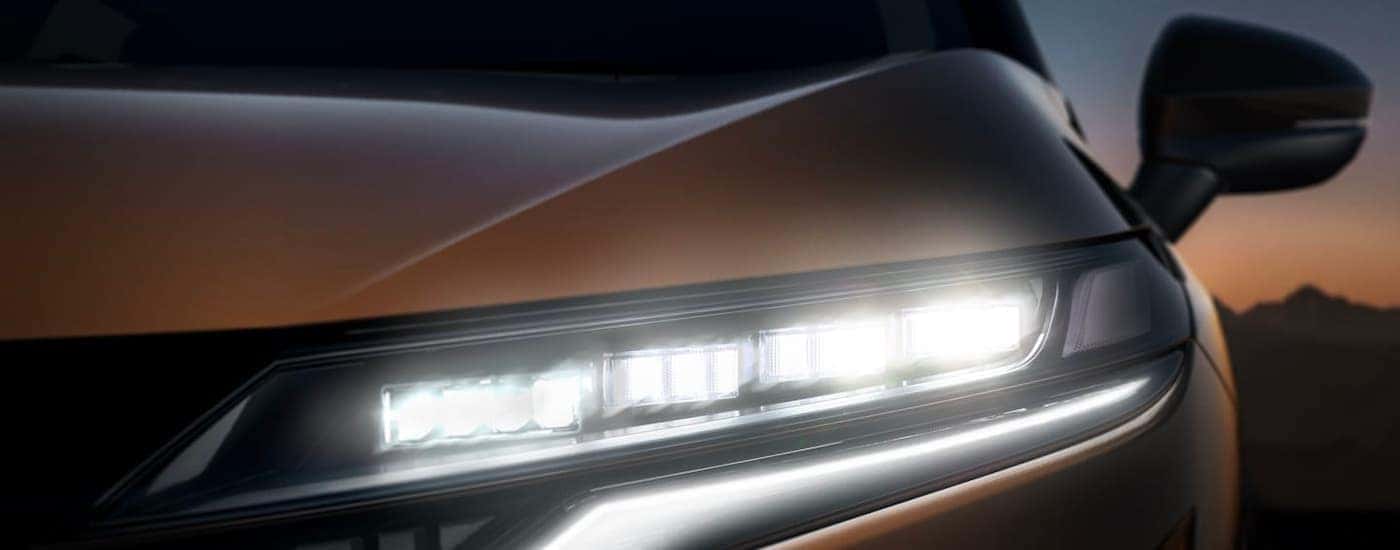 A close up shows the driver side headlight on a bronze 2022 Nissan Ariya.