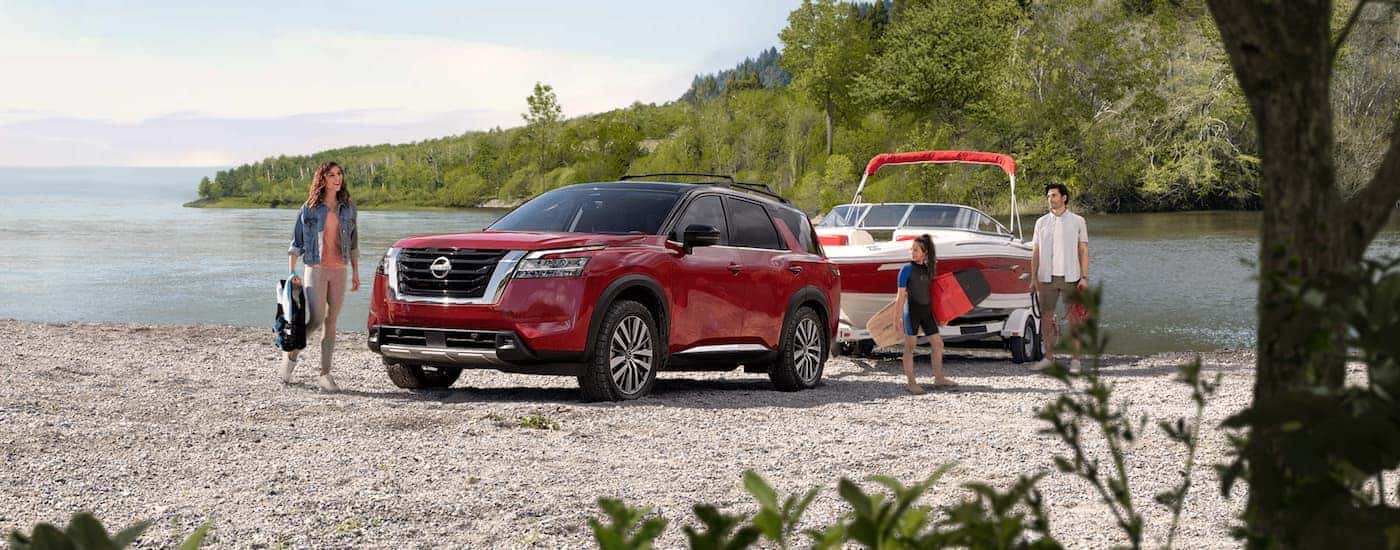 A red 2022 Nissan Pathfinder is shown towing a boat next to a lake.