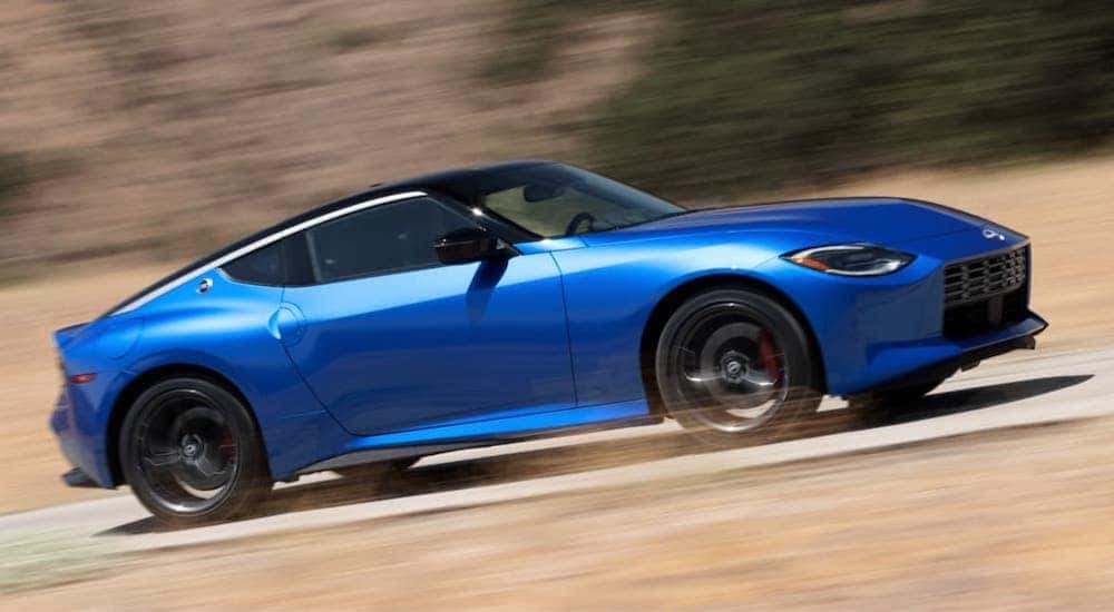 A blue 2023 Nissan Z speeding up a hill with greenery in the background