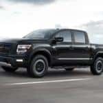 A black 2021 Nissan Titan driving on an empty road with bleak skies