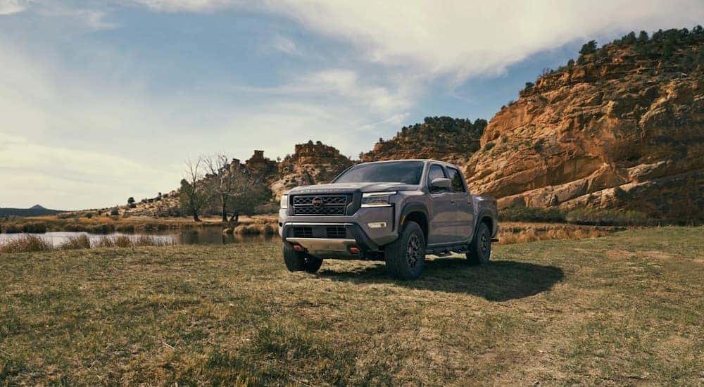 A grey 2023 Nissan Frontier Pro-4x parked in front of cliffs and a lake