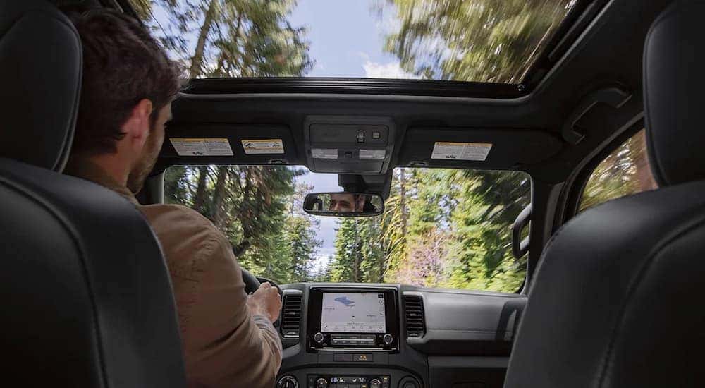 The view of the interior of a 2023 Nissan Frontier from the back seat, with trees seen through the sunroof