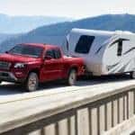 A red 2023 Nissan Frontier is shown from the front at an angle while towing a trailer.