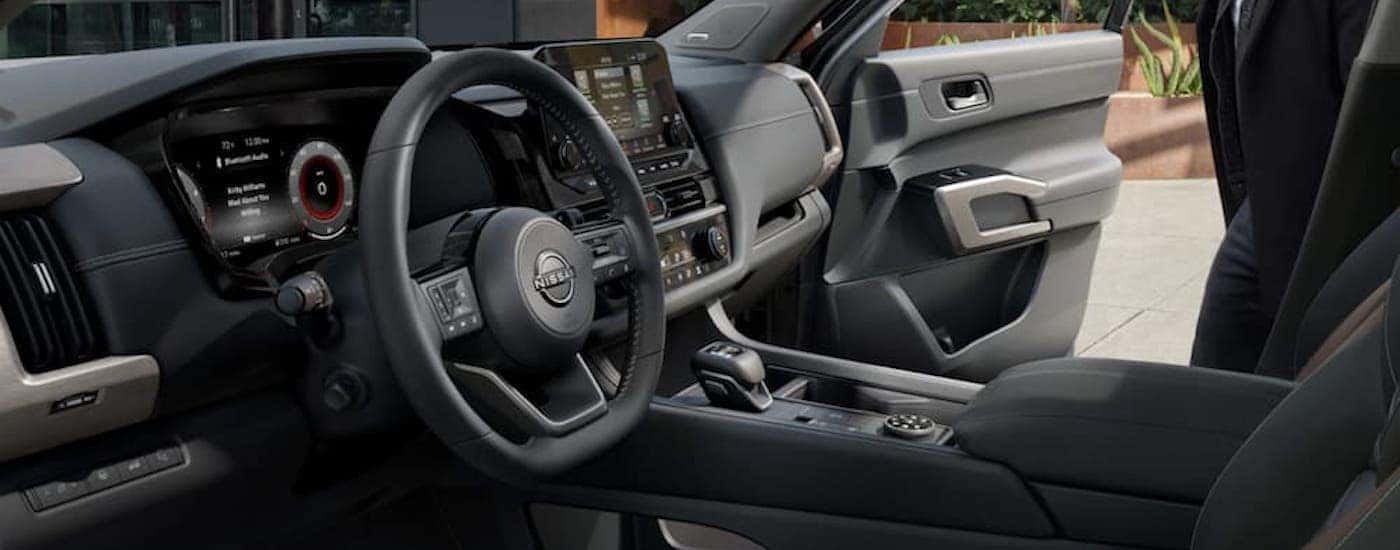 The black interior of a 2023 Nissan Pathfinder shows the steering wheel and infotainment screen.