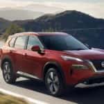 A red 2023 Nissan Rogue drives on a winding mountain road