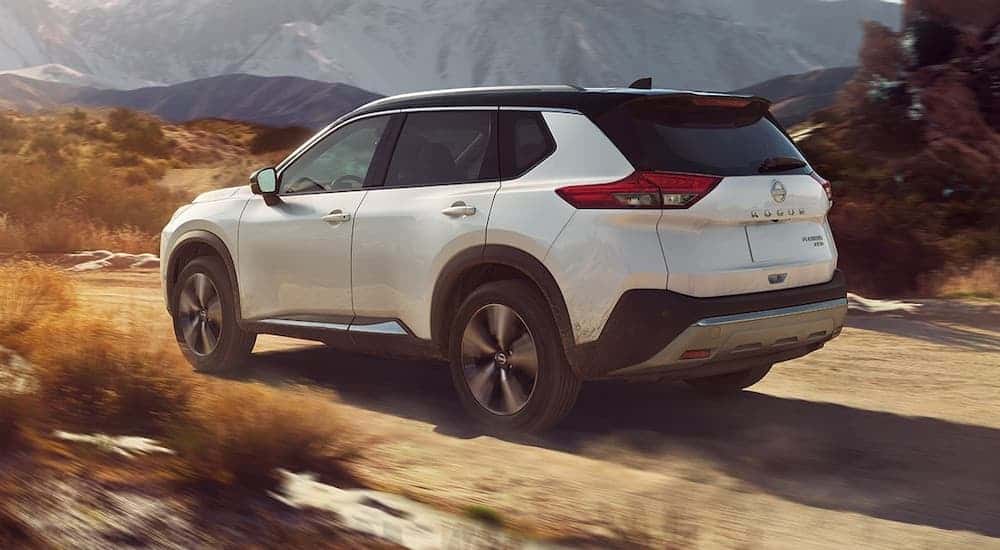 Rear view of a white 2023 Nissan Rogue driving on a desert road