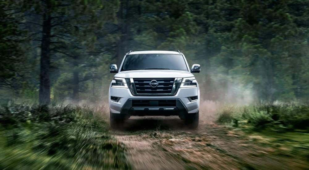 A white 2023 Nissan Armada speeds down a dusty dirt path in the woods