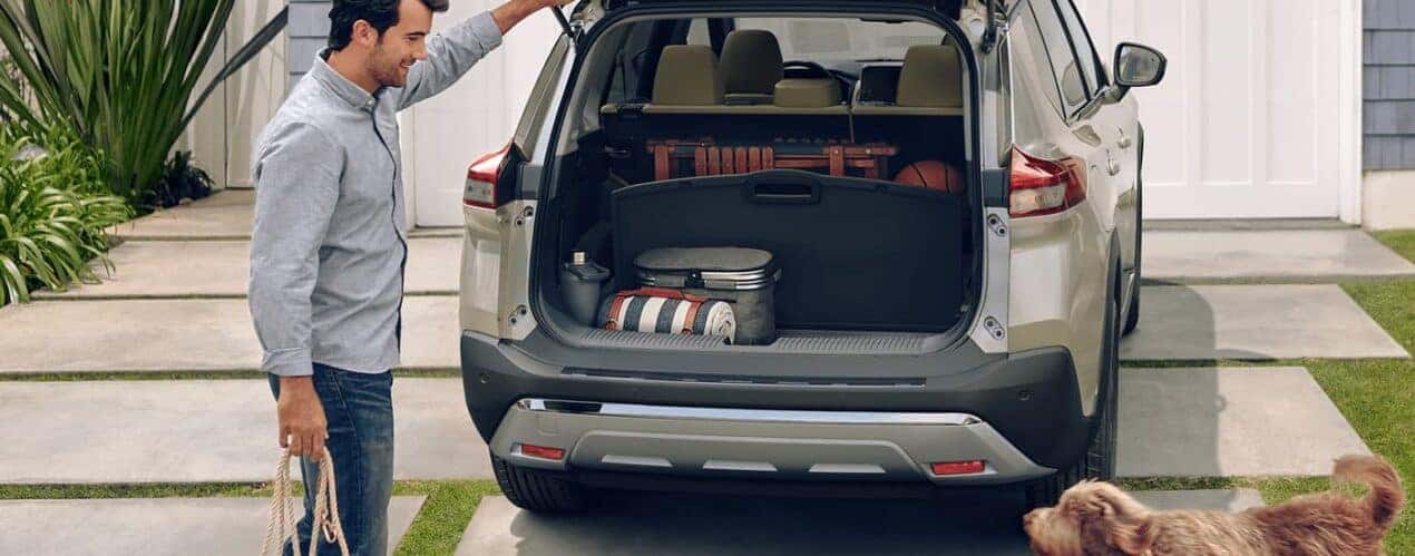 A man is shown shutting the lift-gate of a tan 2023 Nissan Rogue during a 2023 Nissan Rogue vs 2023 Subaru Forester comparison.