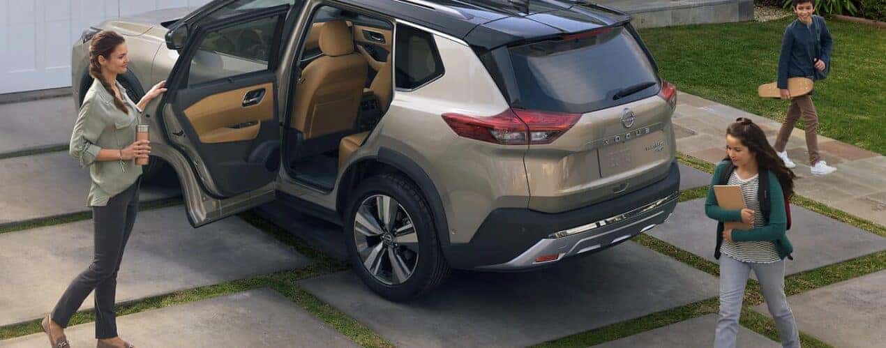 A tan 2023 Nissan Rogue Platinum is shown parked in a driveway next to a family.