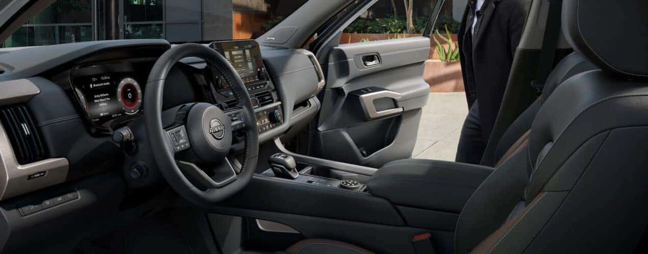 The black interior of a 2023 Nissan Pathfinder shows the steering wheel and front seating.
