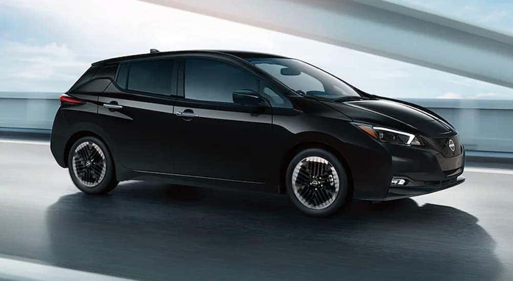 A black 2024 Nissan LEAF is shown driving on a bridge.