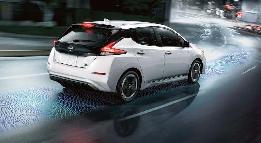 A white 2024 Nissan LEAF is shown driving on a city street.