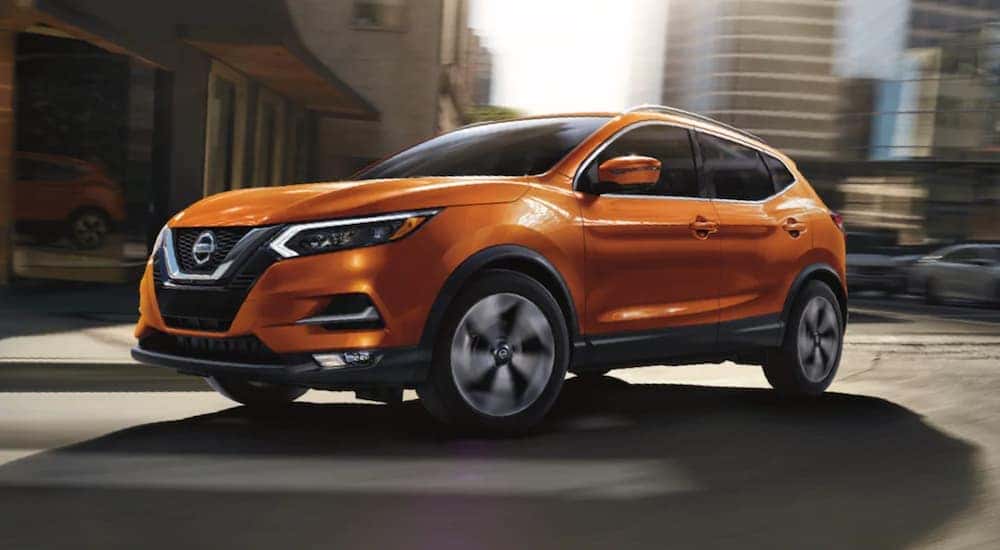 An orange 2020 Nissan Rogue Sport for sale near Hendersonville is shown driving on a city street.
