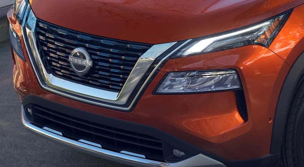 A close-up of the front end of an orange 2024 Nissan Rogue is shown.