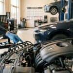A modern automotive service bay interior, warm natural light. A gloved technician's hands (no identifiable faces) inspect the open engine bay of a clean late-model compact sedan, fuel injector rail and intake manifold visible in sharp focus. Neatly organized tools on a rolling cart in the soft-focus background. Photorealistic, shallow depth of field, professional dealership service department atmosphere. No text, no logos other than natural vehicle badging, no identifiable faces. (Representative image for illustration purposes only. Actual vehicle may vary based on trim and configuration.)